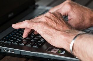 Grafika przedstawia seniora piszącego na laptopie.