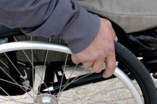 Grafika przedstawia osobę na wózku inwalidzkim. 