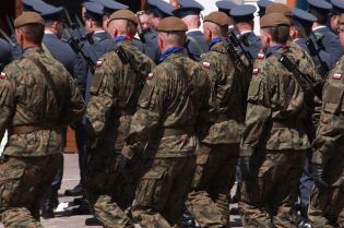 Grafika przedstawia żołnierzy Wojska Polskiego stojących na placu. Widok na żołnierzy jest od tyły.
