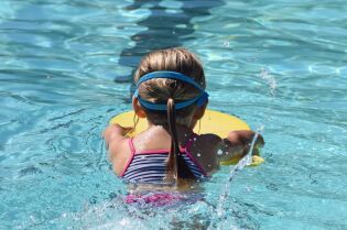 Grafika przedstawia dziewczynkę pływającą w basenie.